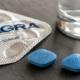Compresse blu di Viagra accanto alla confezione del farmaco e a un bicchiere d’acqua.