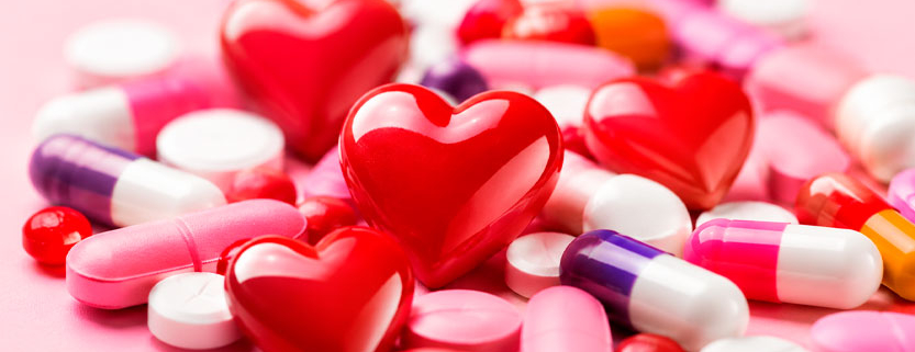 Cuori rossi circondati da compresse e capsule colorate, rappresentazione simbolica del rapporto tra amore e farmaci.