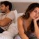 Coppia adulta seduta sul letto, distante e annoiata, con lo sguardo rivolto in direzioni opposte.