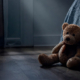 Orsetto di peluche abbandonato sul pavimento accanto a un letto in una stanza buia