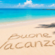 Spiaggia tropicale con mare cristallino, palme e scritta Buone Vacanze sulla sabbia