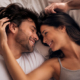 Coppia adulta sdraiata sul letto si guarda sorridendo e si accarezza reciprocamente i capelli